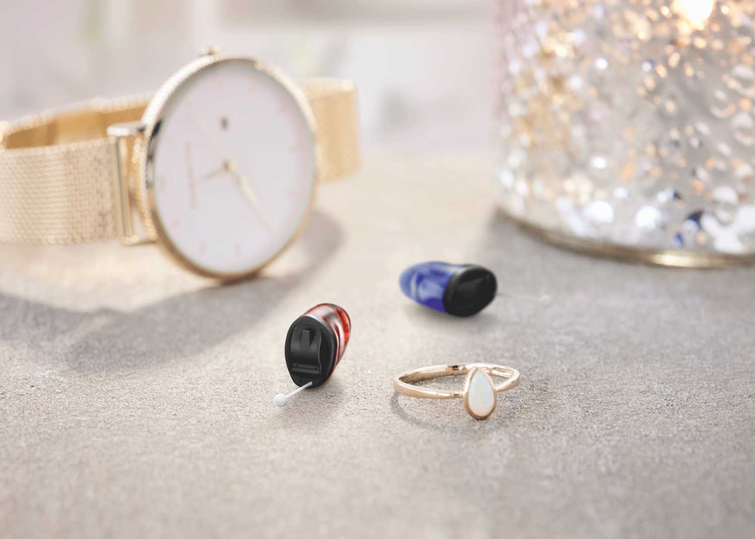 blaues und rotes Hörgerät neben einem Ring und einer eleganten Uhr